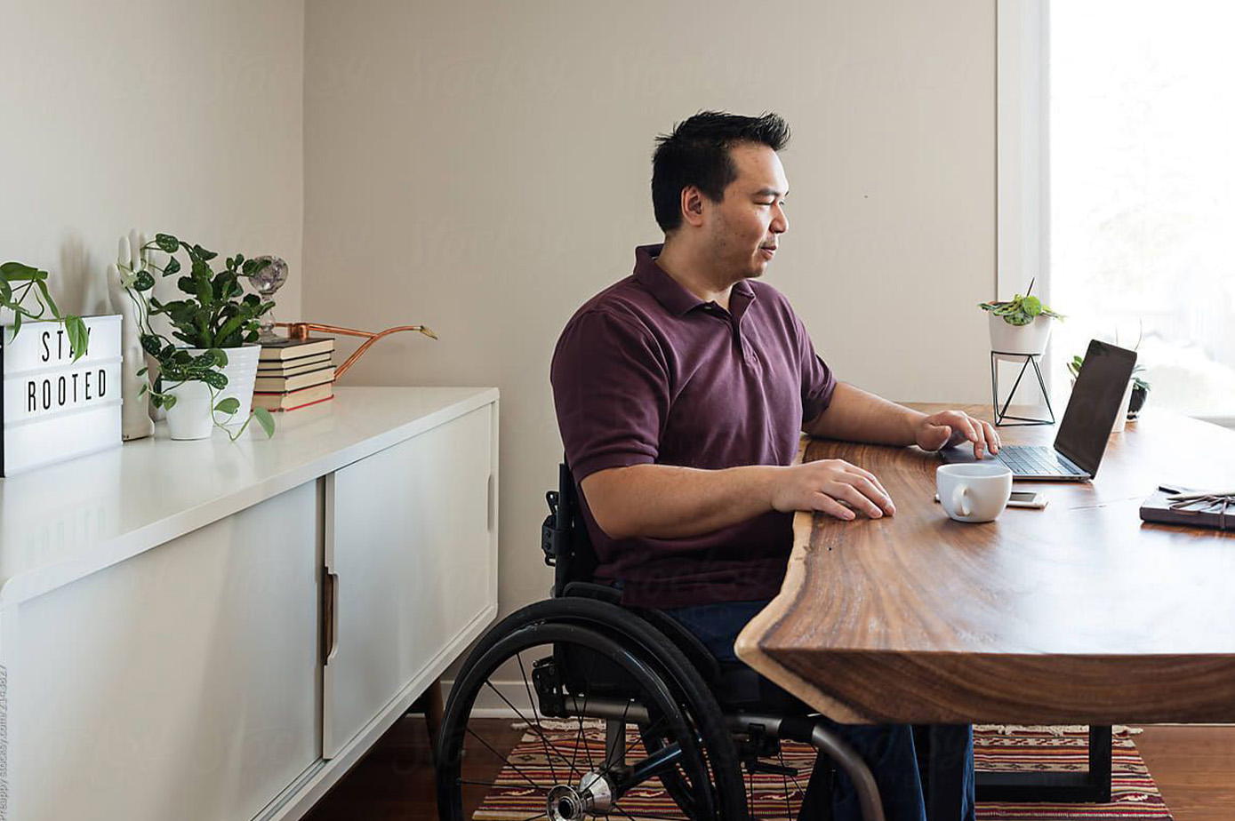 Picture of a person in wheelchair sitting at a desk, working on a computer